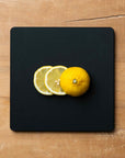 Lemons on a black square cutting board on a wooden surface
